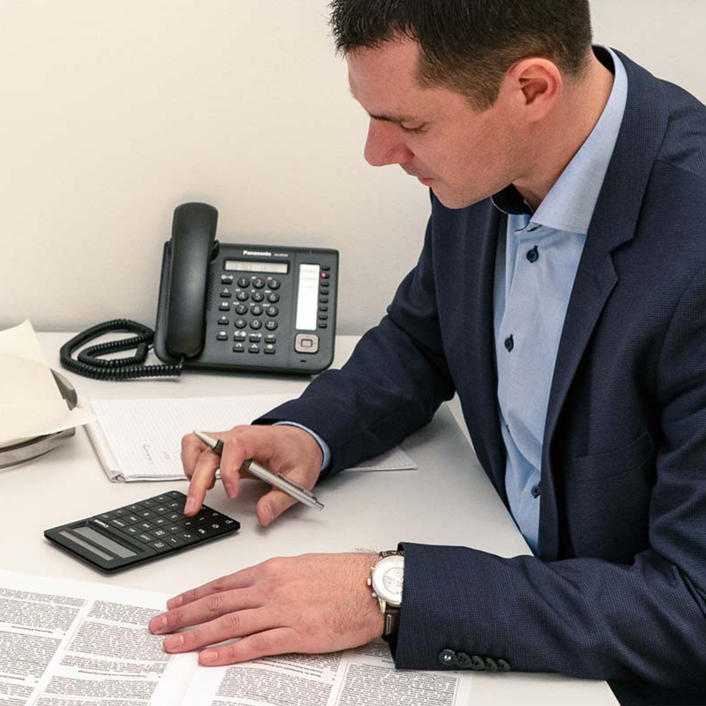 Andreas Bardelli sitzt am Schreibtisch und tippt etwas in einen Taschenrechner ein.